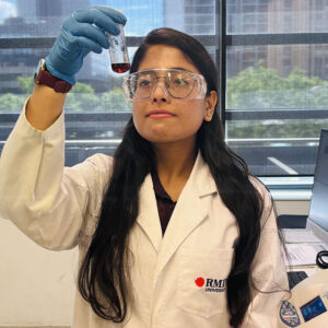 Female BITS-RMIT academy PhD candidate holding a small glass containing a red solution inside a research laboratory settings.