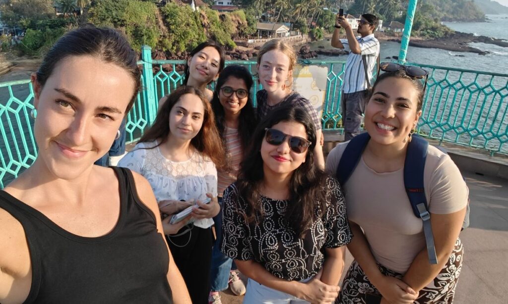 Group of students smiling and taking a selfie together on a pier overlooking water.